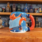 The right side view of a handmade Knight Helmet Mug with a light blue, blue and red-orange armour design, featuring dark blue ornamental rivets and a detailed red handle.