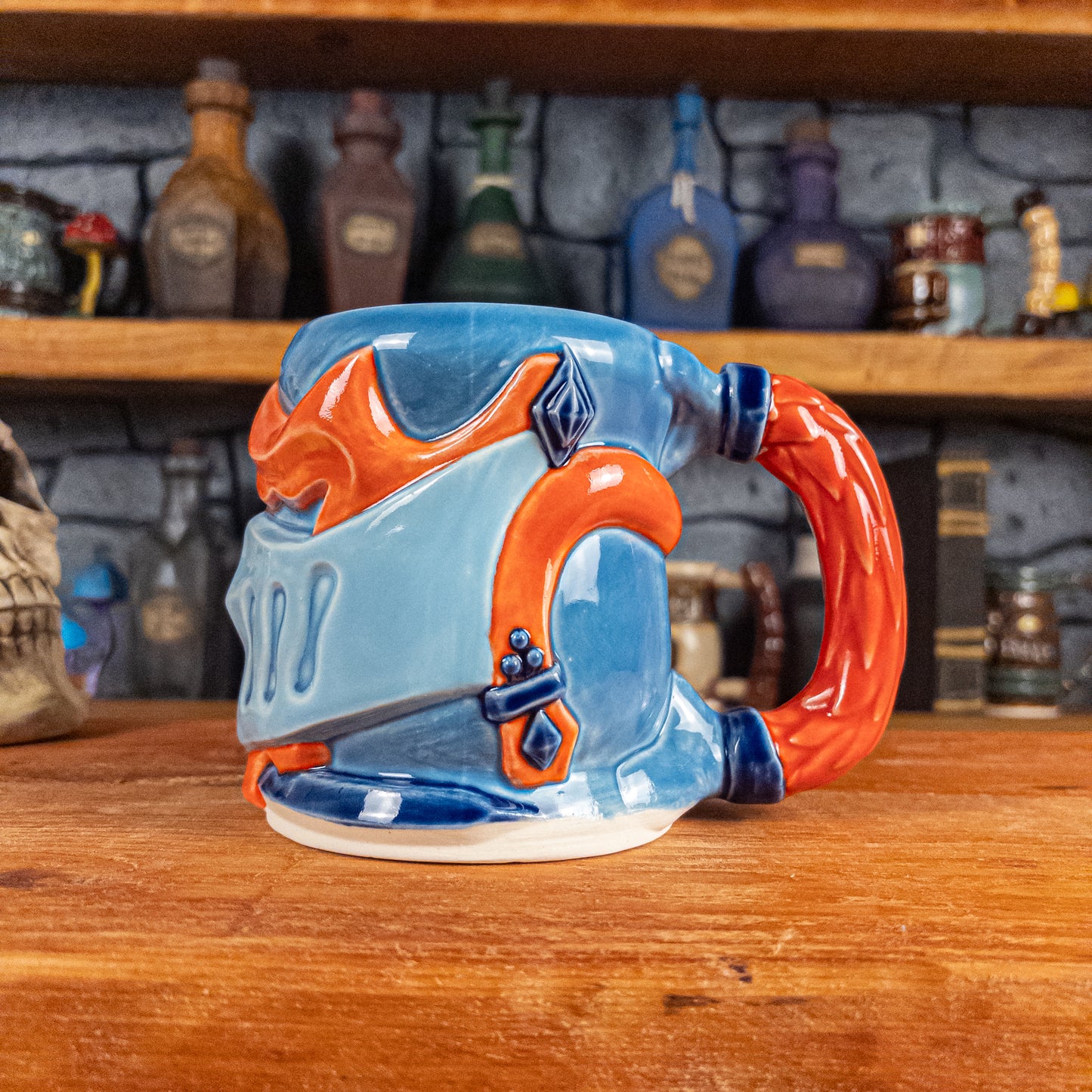The right side view of a handmade Knight Helmet Mug with a light blue, blue and red-orange armour design, featuring dark blue ornamental rivets and a detailed red handle.