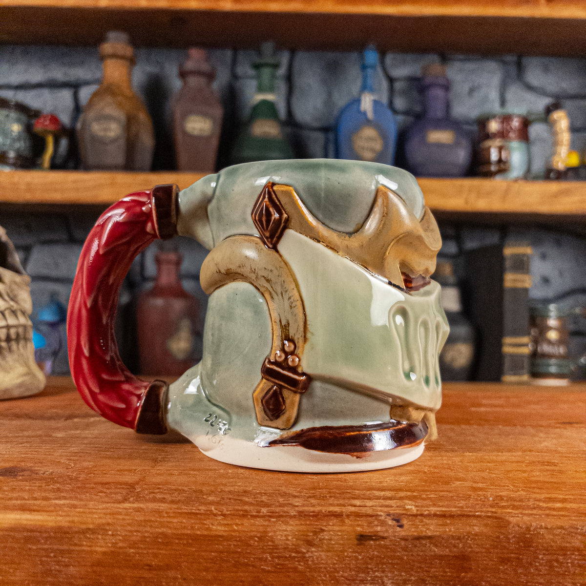The left side view of a handmade Knight Helmet Mug with a beige and semi-transparent green armour design and brown eye slits, featuring ornamental rivets and a detailed red handle.