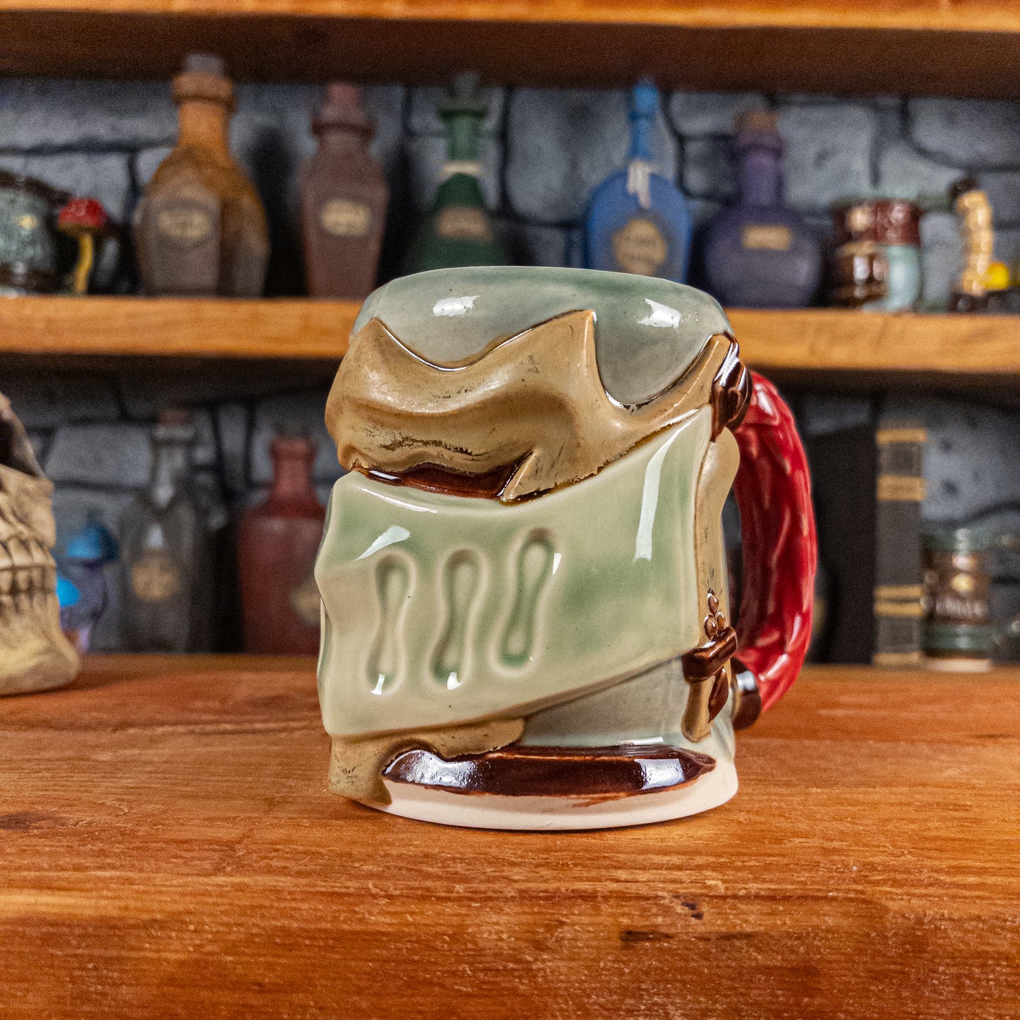 Three-quarter right side view of a handmade Knight Helmet Mug with a beige and semi-transparent green armour design and brown eye slits, featuring ornamental rivets and a detailed red handle.