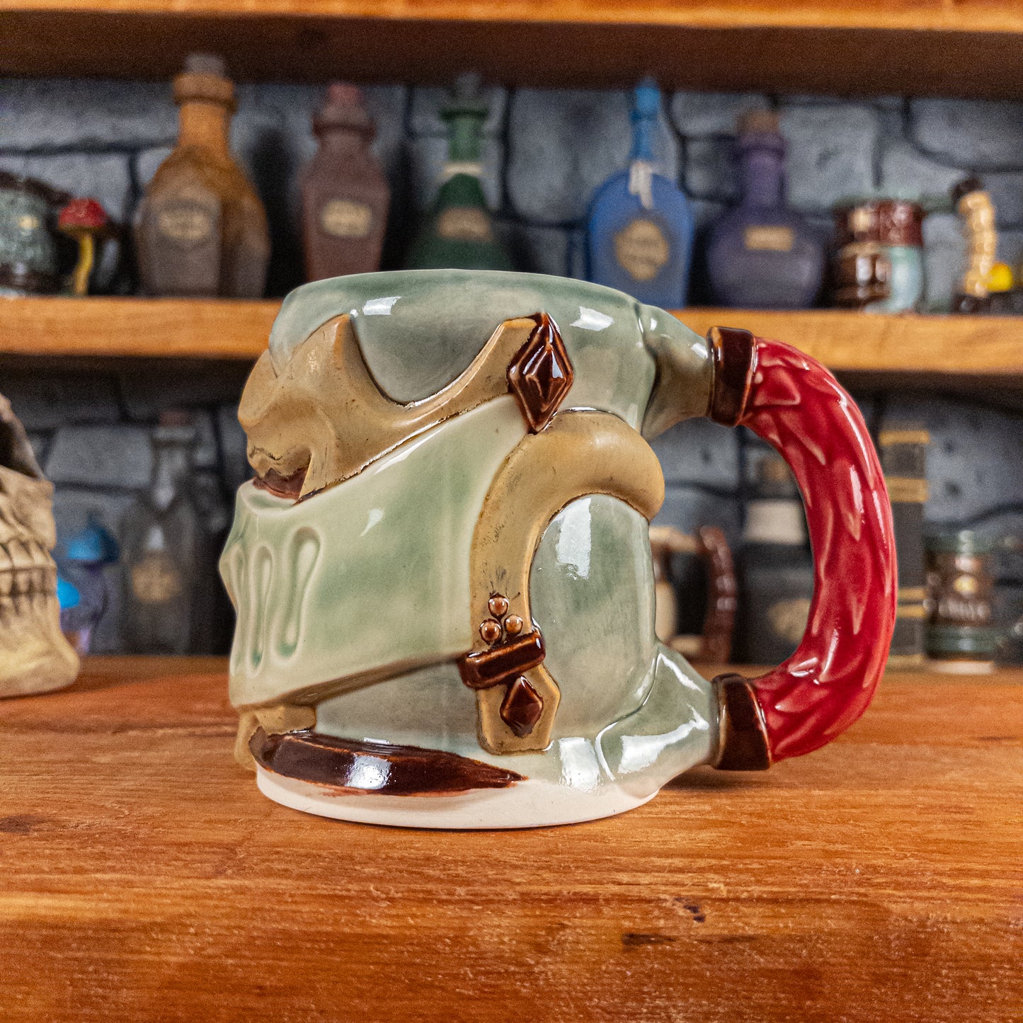 The right side view of a handmade Knight Helmet Mug with a beige and semi-transparent green armour design and brown eye slits, featuring ornamental rivets and a detailed red handle.