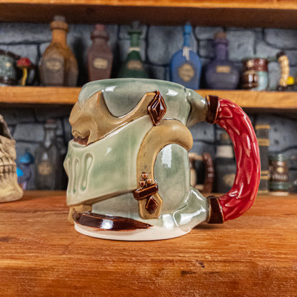 The right side view of a handmade Knight Helmet Mug with a beige and semi-transparent green armour design and brown eye slits, featuring ornamental rivets and a detailed red handle.