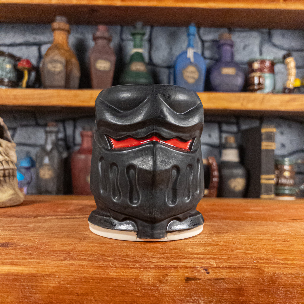 Front view of a handmade Knight Helmet Mug with a matte black armour design and glossy red eye slits.