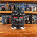 Front view of a handmade Knight Helmet Mug with a matte black armour design and glossy red eye slits.