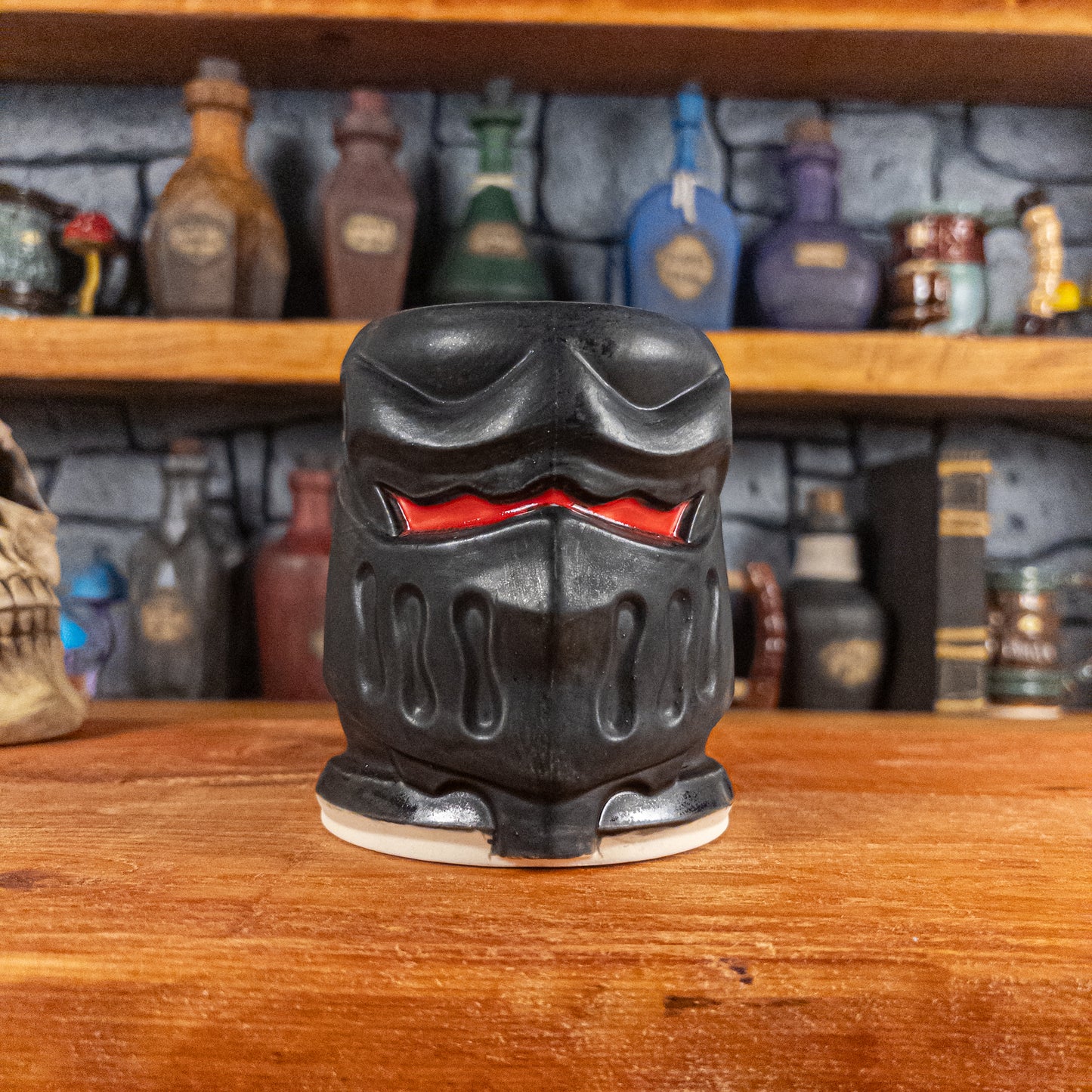 Front view of a handmade Knight Helmet Mug with a matte black armour design and glossy red eye slits.