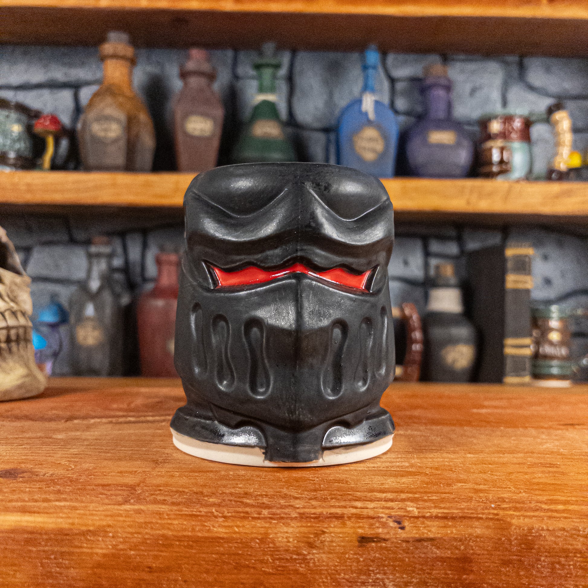 Front view of a handmade Knight Helmet Mug with a matte black armour design and glossy red eye slits.