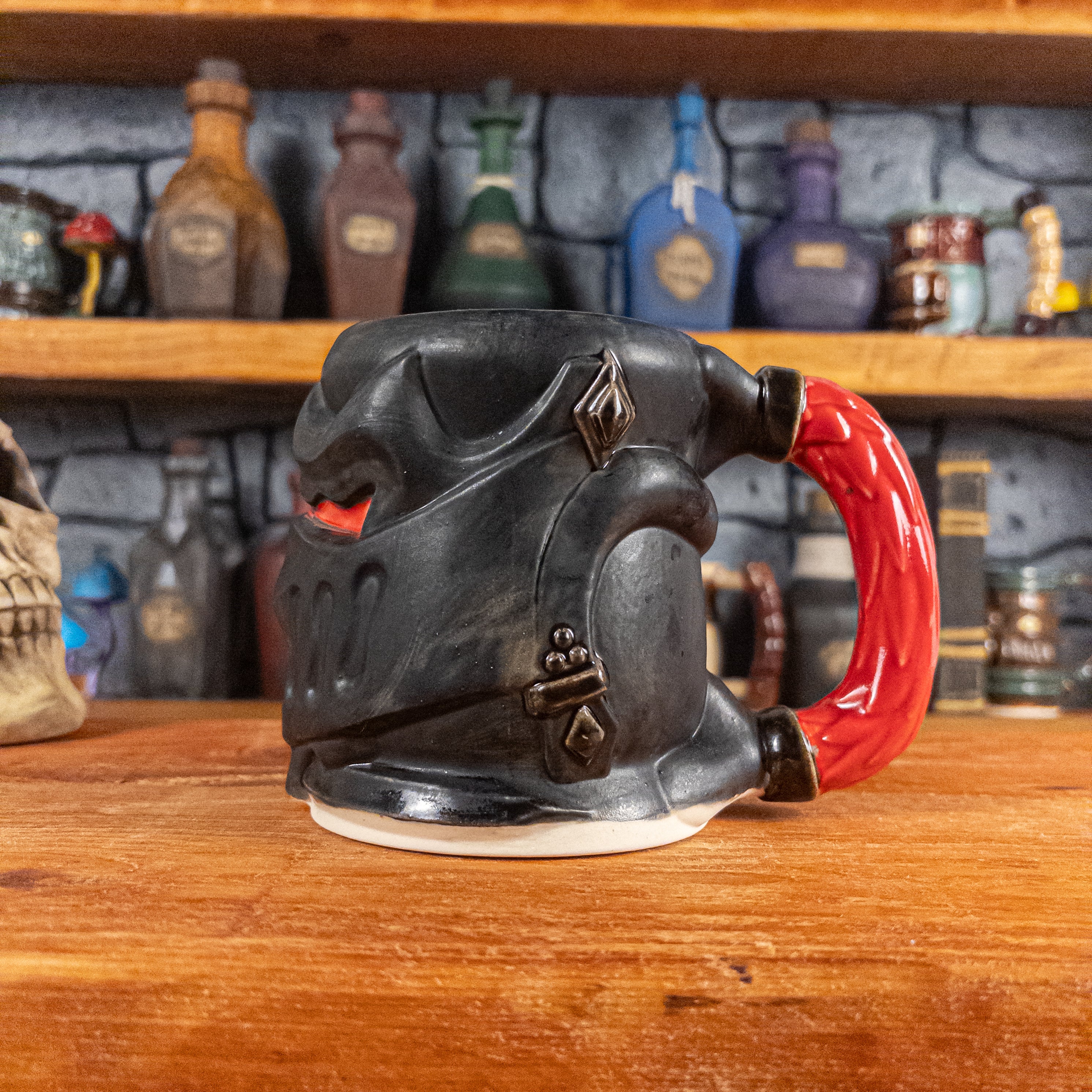 The right side view of a handmade Knight Helmet Mug with a matte black armour design and glossy red eye slits, featuring ornamental rivets and a detailed red handle.