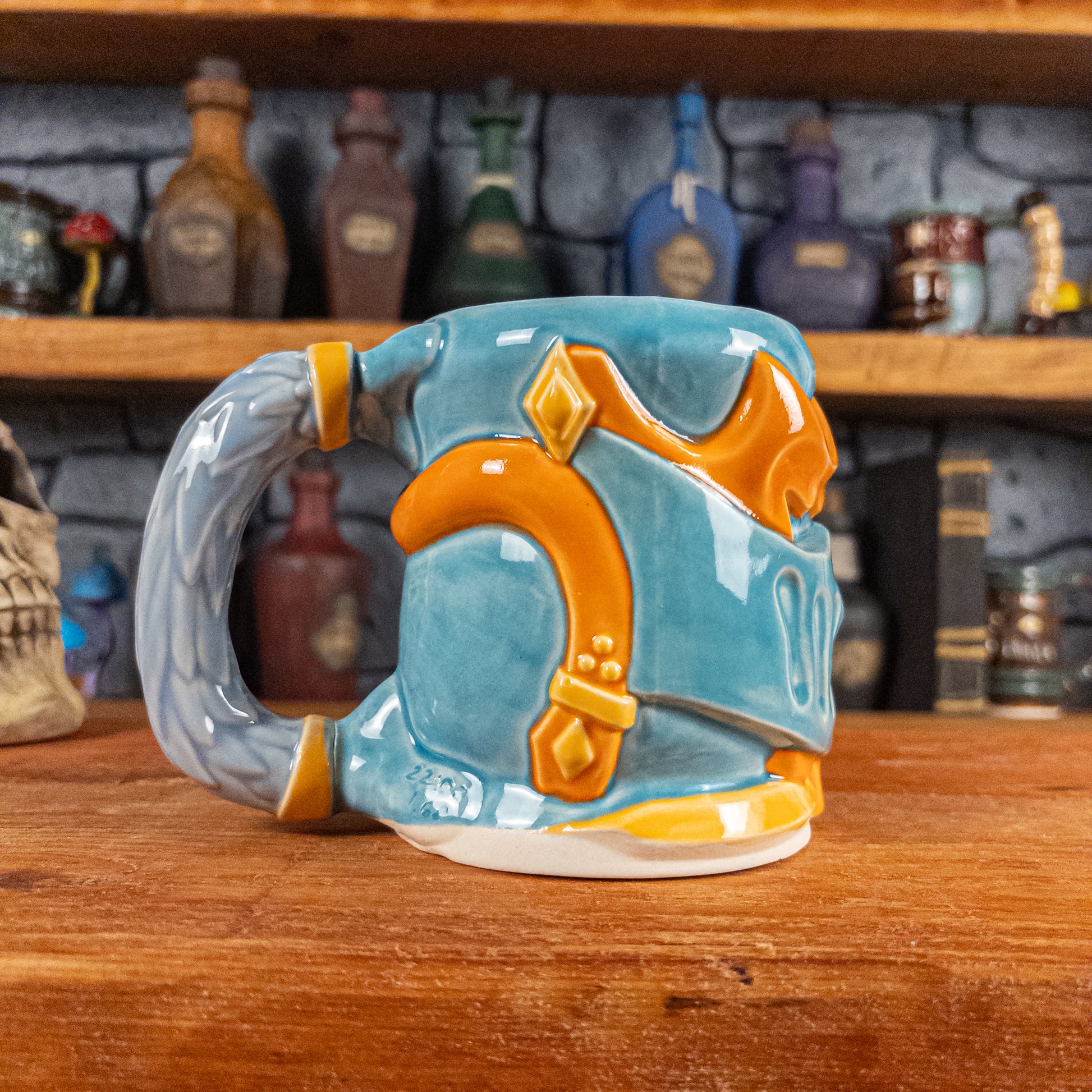 The left side view of a handmade Knight Helmet Mug with a light blue and orange armour design, featuring ornamental rivets and a detailed light dusty blue handle.