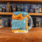 Three-quarter right side view of a handmade Knight Helmet Mug with a light blue and orange armour design, featuring ornamental rivets and a detailed light dusty blue handle.