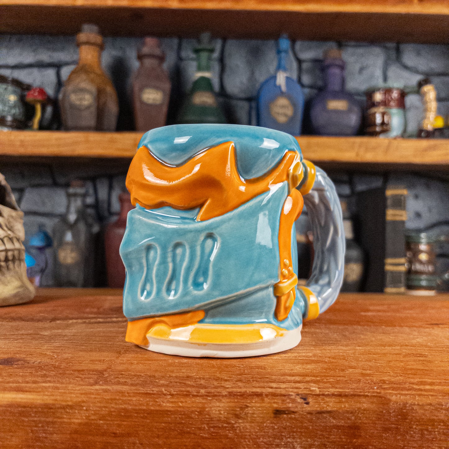 Three-quarter right side view of a handmade Knight Helmet Mug with a light blue and orange armour design, featuring ornamental rivets and a detailed light dusty blue handle.