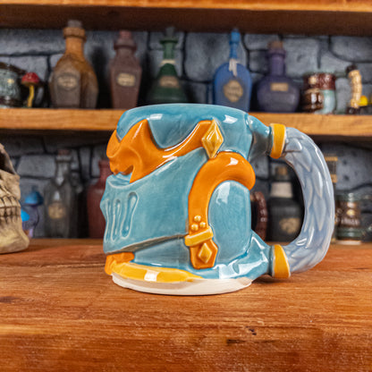 The right side view of a handmade Knight Helmet Mug with a light blue and orange armour design, featuring ornamental rivets and a detailed light dusty blue handle.