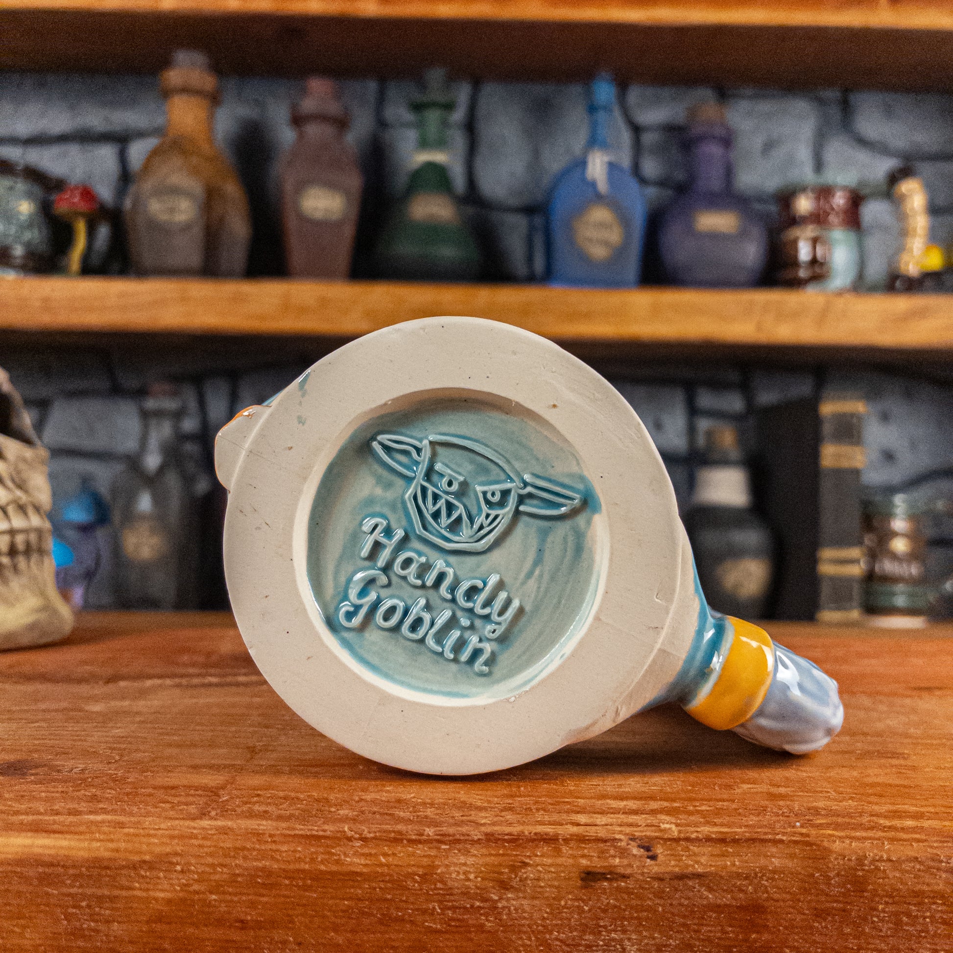 Bottom view of a handmade Knight Helmet Mug with the Handy Goblin logo embossed in the centre, featuring a light blue base.