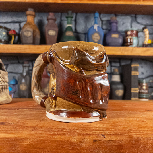 Three-quarter left side view of a handmade Knight Helmet Mug with a brown and rusted armour design and brown eye slits, featuring ornamental rivets and a detailed sandy handle.