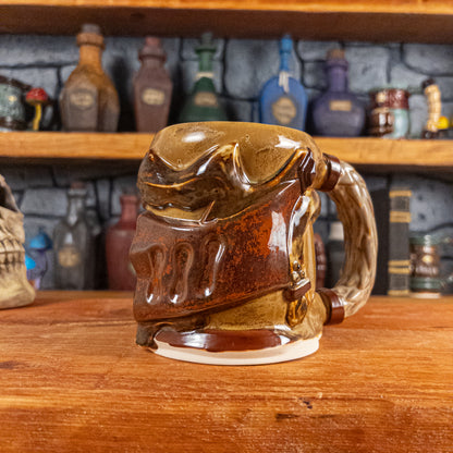 Three-quarter right side view of a handmade Knight Helmet Mug with a brown and rusted armour design and brown eye slits, featuring ornamental rivets and a detailed sandy handle.
