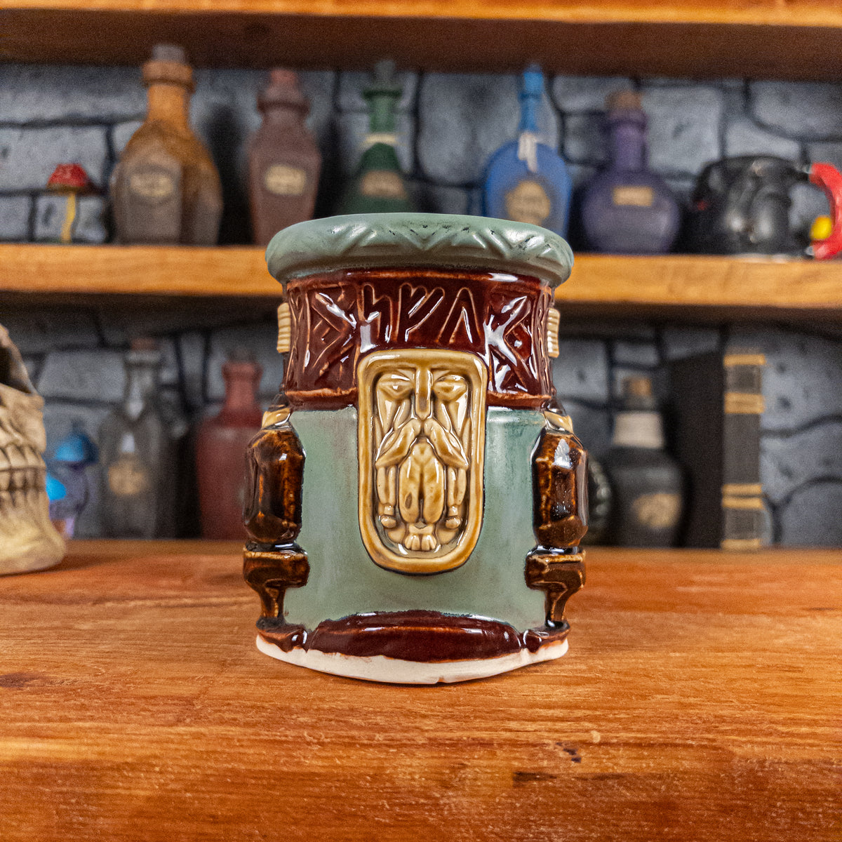 Front view of a handmade Dwarven Mug designed to look like a greenish-blue and dark red barrel with intricate rune carvings, a dark beige dwarf face, and a partial hammer and anvil design.
