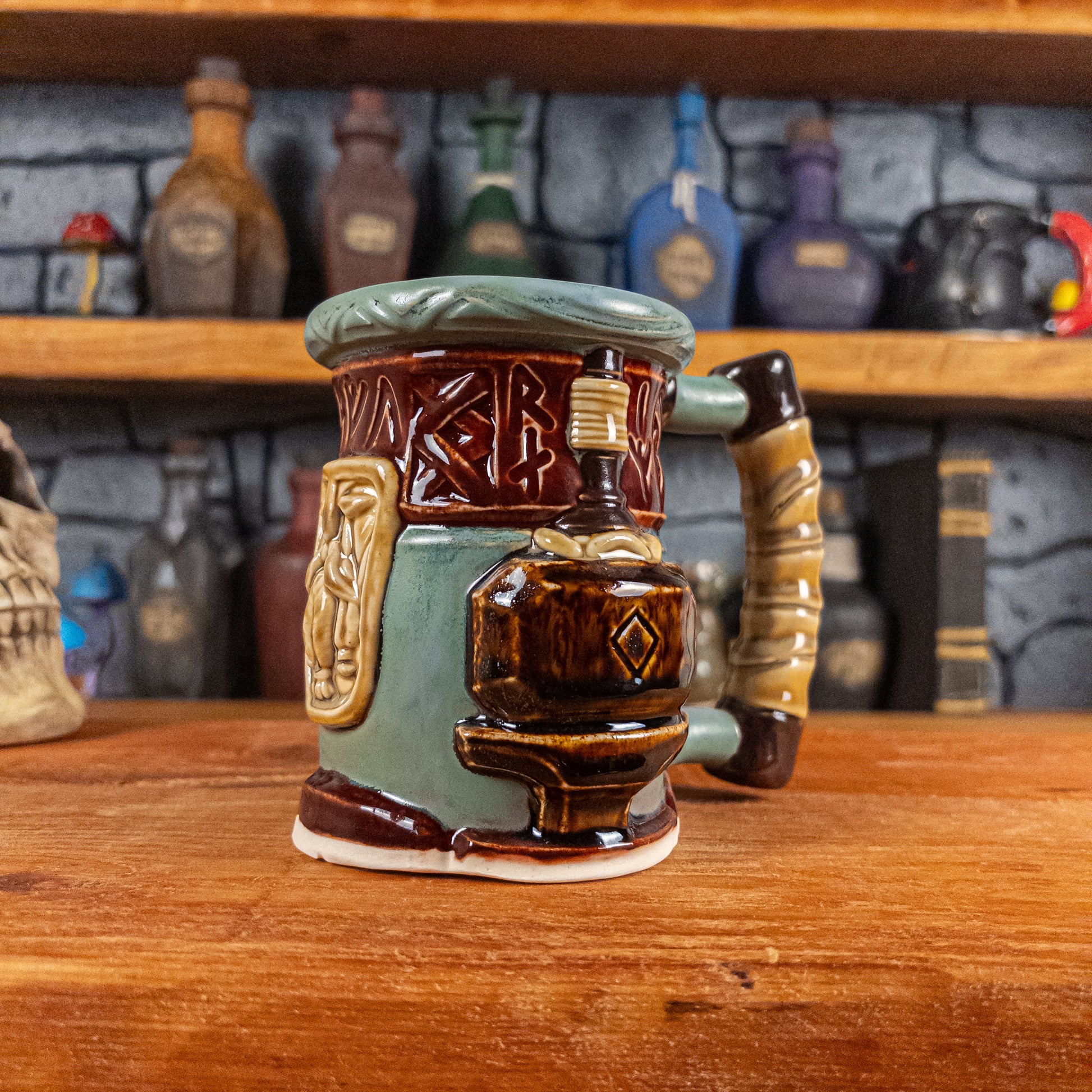Three-quarter right side view of a handmade Dwarven Mug designed to look like a greenish-blue and dark red barrel with intricate rune carvings, a dark beige dwarf face, and a hammer and anvil design, showing the detailed handle.