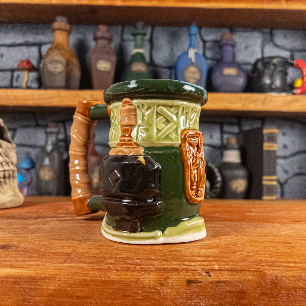 Three-quarter left side view of a handmade Dwarven Mug designed to look like a light and dark green barrel with intricate rune carvings, a light brown dwarf face, and a hammer and anvil design, showing the detailed handle.