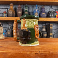 Three-quarter left side view of a handmade Dwarven Mug designed to look like a light and dark green barrel with intricate rune carvings, a light brown dwarf face, and a hammer and anvil design, showing the detailed handle.