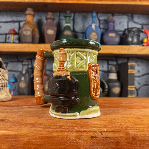 Three-quarter left side view of a handmade Dwarven Mug designed to look like a light and dark green barrel with intricate rune carvings, a light brown dwarf face, and a hammer and anvil design, showing the detailed handle.