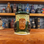 Front view of a handmade Dwarven Mug designed to look like a light and dark green barrel with intricate rune carvings, a light brown dwarf face, and a partial hammer and anvil design.