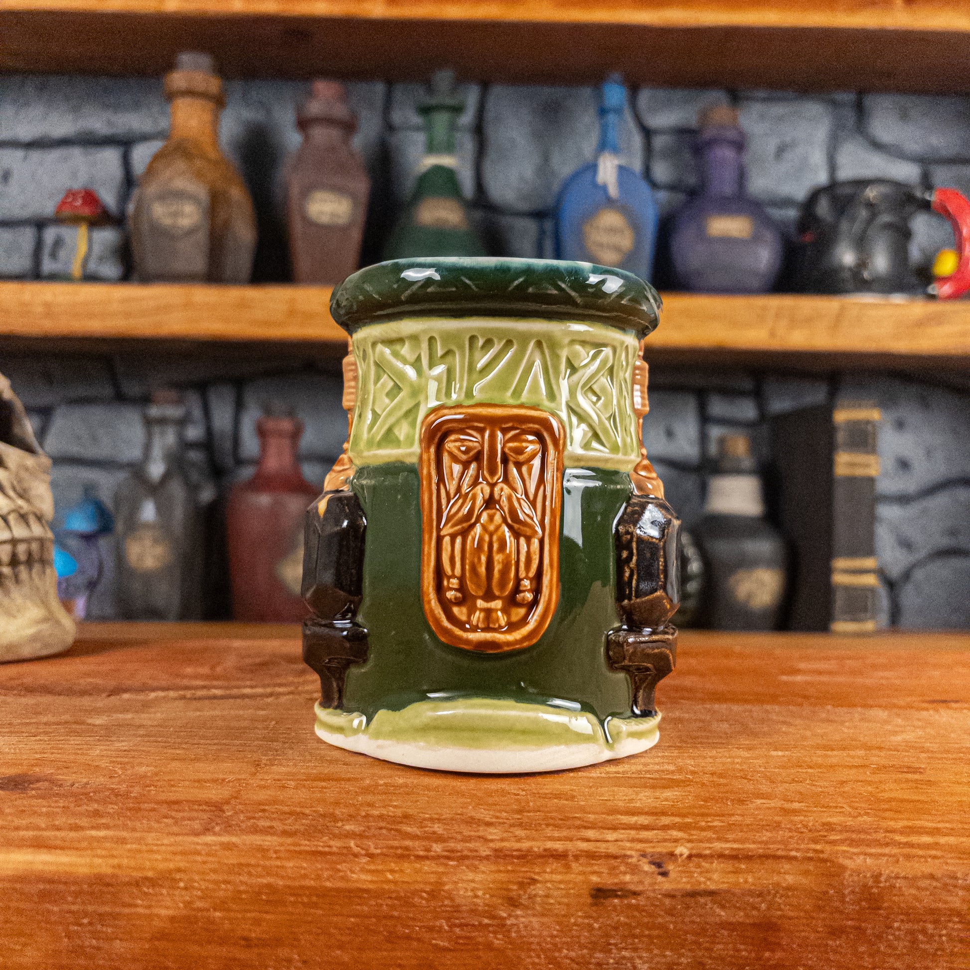 Front view of a handmade Dwarven Mug designed to look like a light and dark green barrel with intricate rune carvings, a light brown dwarf face, and a partial hammer and anvil design.