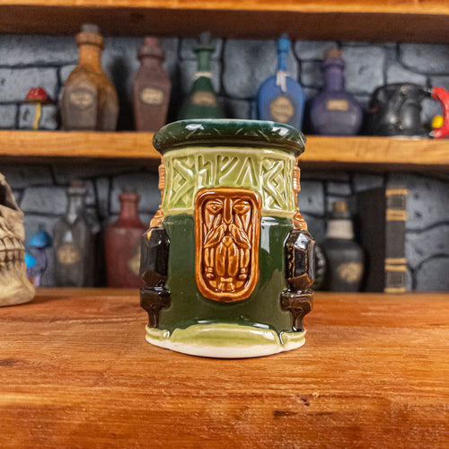 Front view of a handmade Dwarven Mug designed to look like a light and dark green barrel with intricate rune carvings, a light brown dwarf face, and a partial hammer and anvil design.