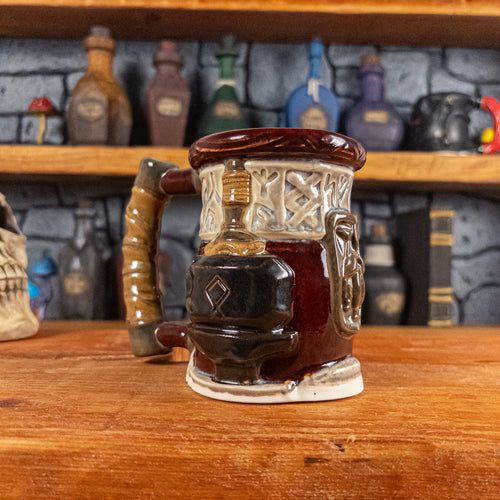 Three-quarter left side view of a handmade Dwarven Mug designed to look like a wine red and light sand barrel with intricate rune carvings, a dark brown dwarf face, and a hammer and anvil design, showing the detailed handle.