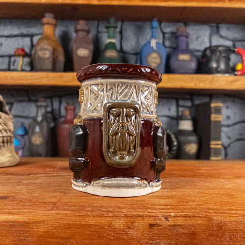 Front view of a handmade Dwarven Mug designed to look like wine red and light sand barrel with intricate rune carvings, a dark brown dwarf face, and a partial hammer and anvil design.