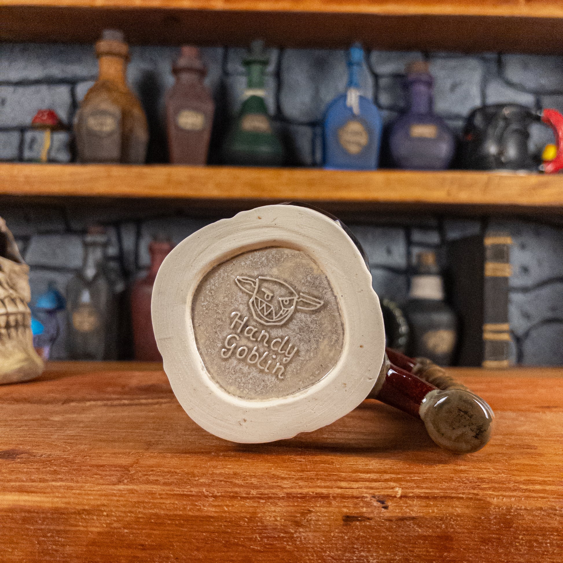 Bottom view of a handmade Dwarven Mug with the 'Handy Goblin' logo embossed in the center, featuring a light sand base.