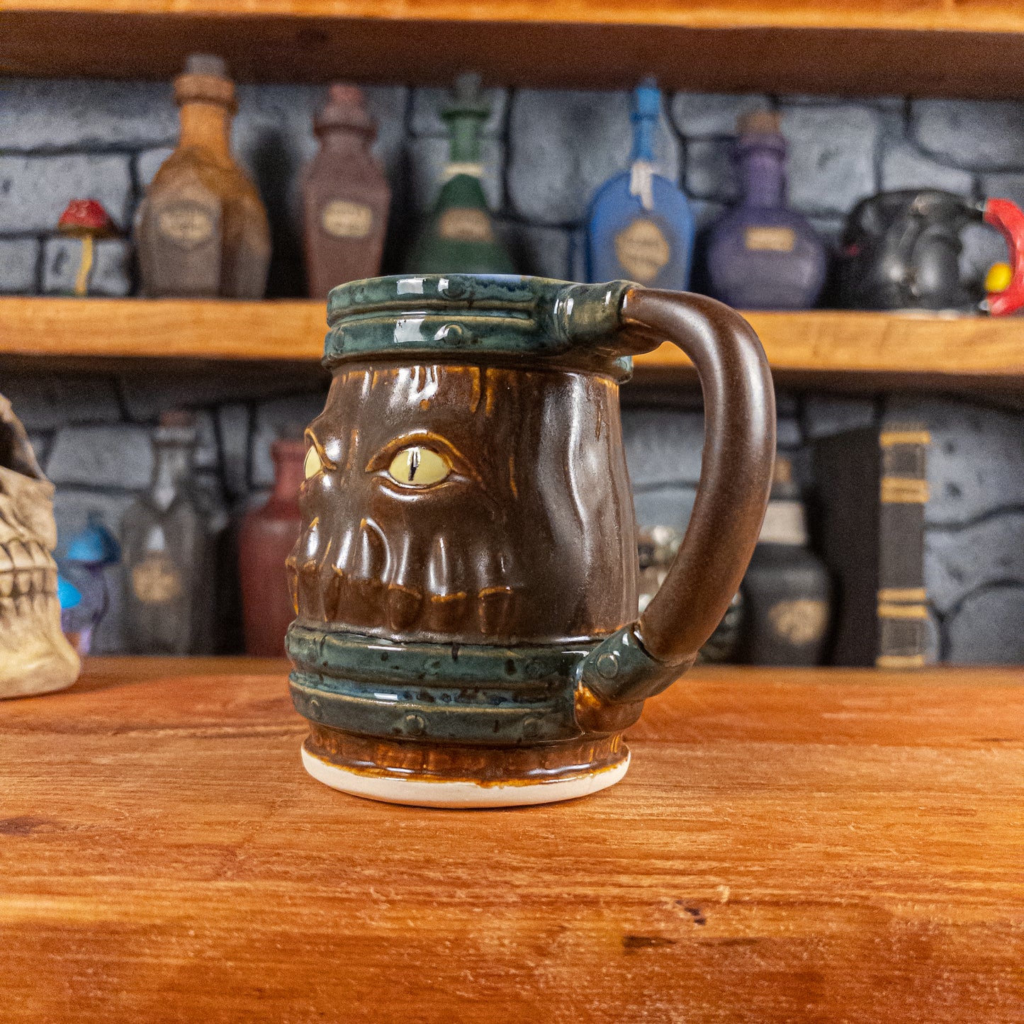 Three-quarter right side view of a handmade Mimic Mug designed to look like a brown wooden barrel with dark green bands, displaying menacing yellow eyes and teeth, and a handle.