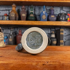 Bottom view of a handmade Mimic Mug with the Handy Goblin logo embossed in the center, featuring a greenish-blue base.