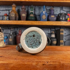 Bottom view of a handmade Mimic Mug with the Handy Goblin logo embossed in the center, featuring a speckled light blue base.