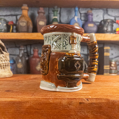 Three-quarter right side view of a handmade Dwarven Mug designed to look like a light green and reddish brown barrel with intricate rune carvings, a dwarf face, and a hammer and anvil design, showing the detailed handle.