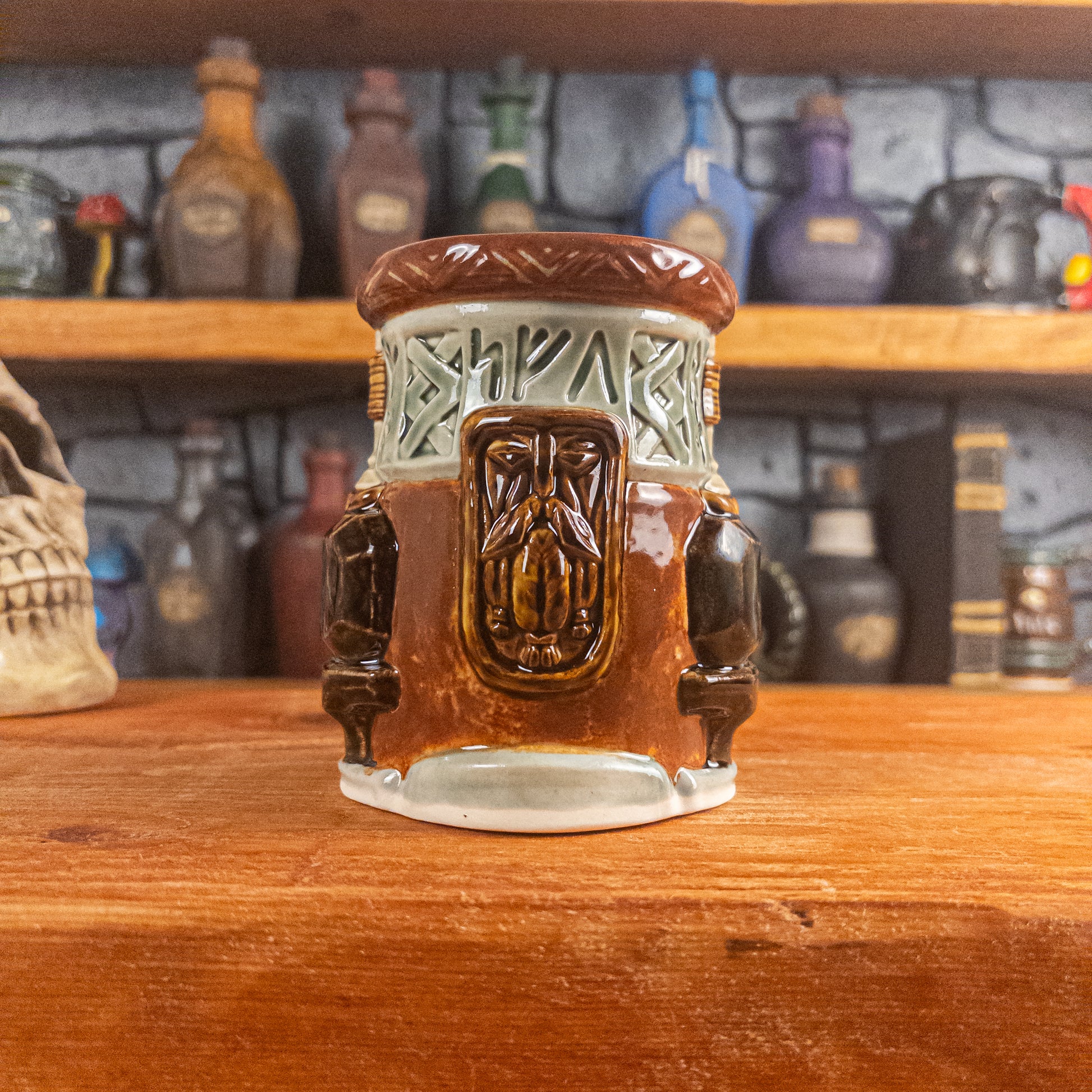 Front view of a handmade Dwarven Mug designed to look like a light green and reddish-brown barrel with intricate rune carvings, a dwarf face, and a partial hammer and anvil design.