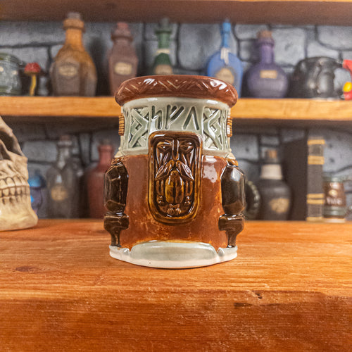 Front view of a handmade Dwarven Mug designed to look like a light green and reddish-brown barrel with intricate rune carvings, a dwarf face, and a partial hammer and anvil design.