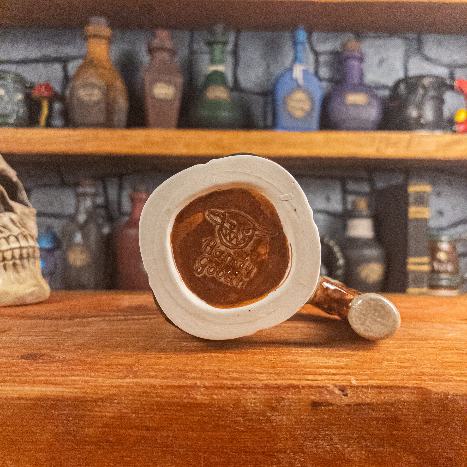 Bottom view of a handmade Dwarven Mug with the 'Handy Goblin' logo embossed in the center, featuring a reddish-brown base.