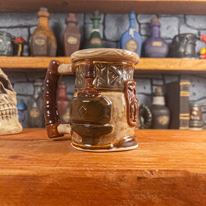 Three-quarter left side view of a handmade Dwarven Mug designed to look like a beige and dark brown barrel with intricate rune carvings, a brown dwarf face, and a hammer and anvil design, showing the detailed handle.