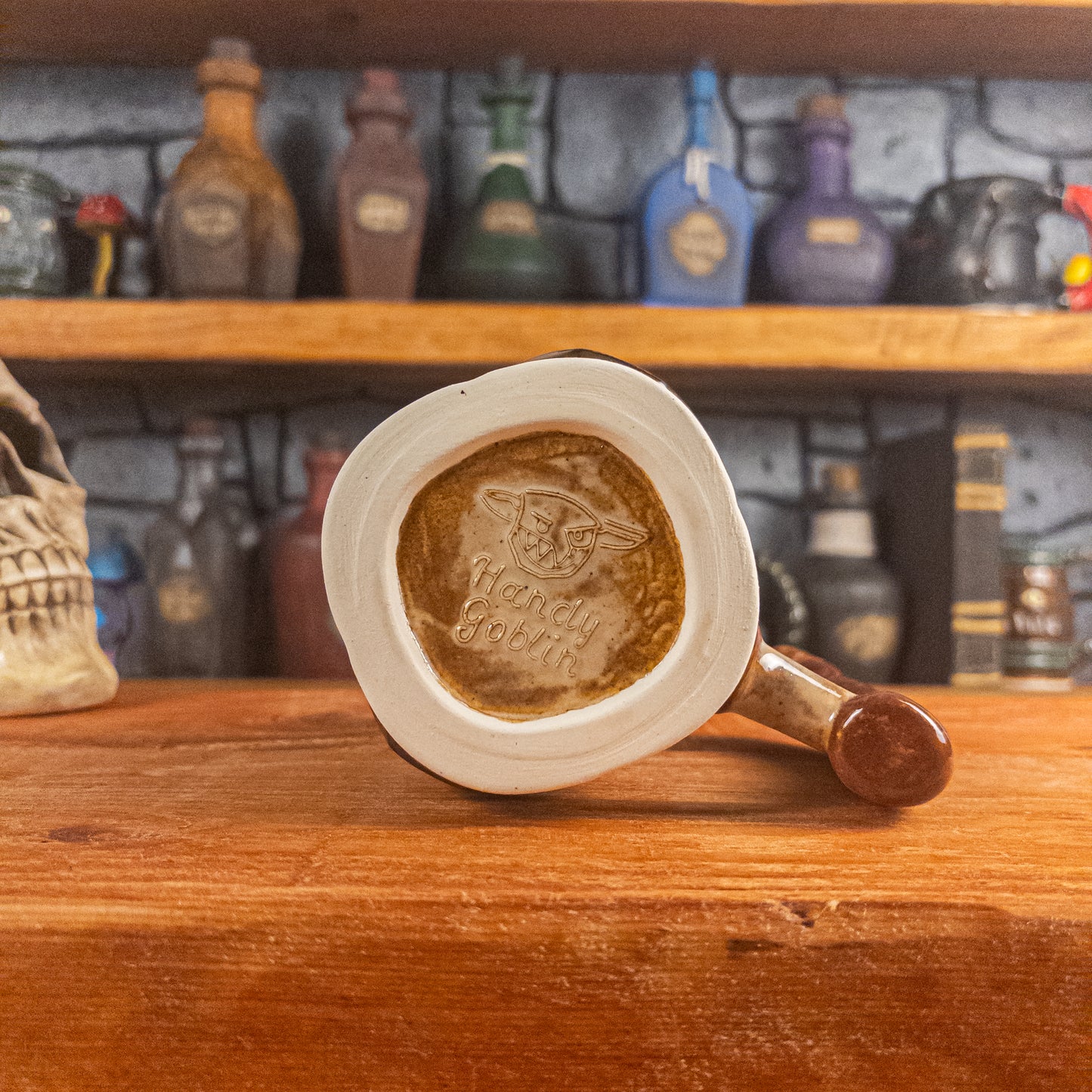 Bottom view of a handmade Dwarven Mug with the 'Handy Goblin' logo embossed in the center, featuring a brown-beige base.