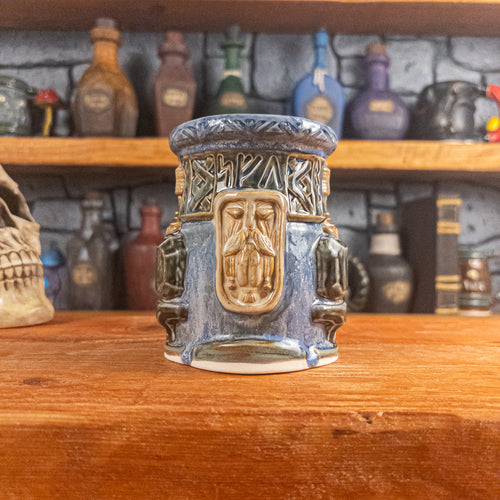 Front view of a handmade Dwarven Mug designed to look like white-blue and brown-blue barrel with intricate rune carvings, a beige dwarf face, and a partial hammer and anvil design.